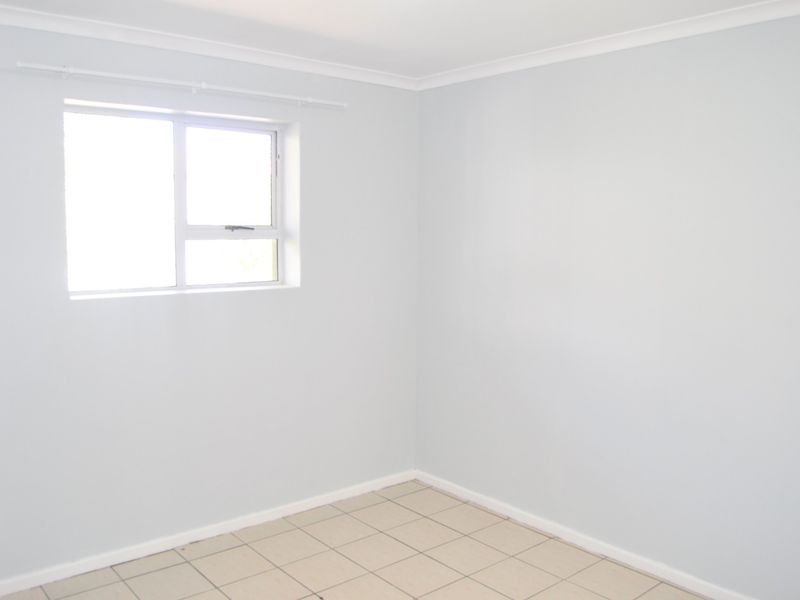 A bright, empty bedroom featuring neutral wall paint, tiled flooring, and a functional sliding window with an installed curtain rod.