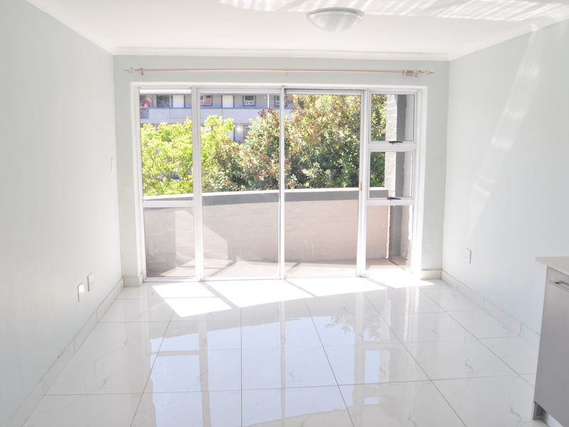 Bright open-plan living area featuring polished white tiled flooring and a large sliding glass door providing access to an outdoor balcony.