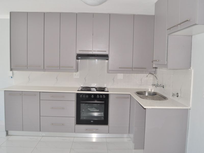 Modern kitchen featuring sleek grey cabinetry, stone countertops, built-in oven, electric hob, extractor fan, and polished tiled flooring.