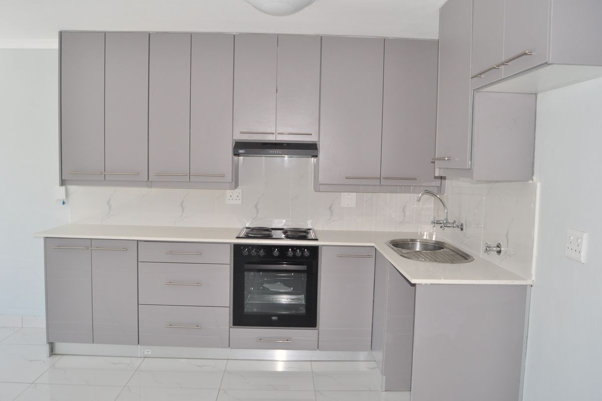 Modern kitchen featuring sleek grey cabinetry, stone countertops, built-in oven, electric hob, extractor fan, and polished tiled flooring.