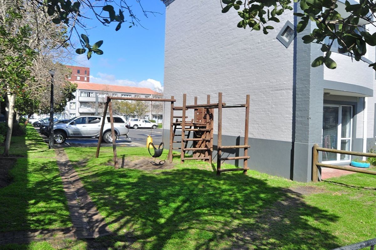 Exterior view of the apartment building featuring a painted brick facade, sliding glass door access, and a shared lawn area with playground equipment.