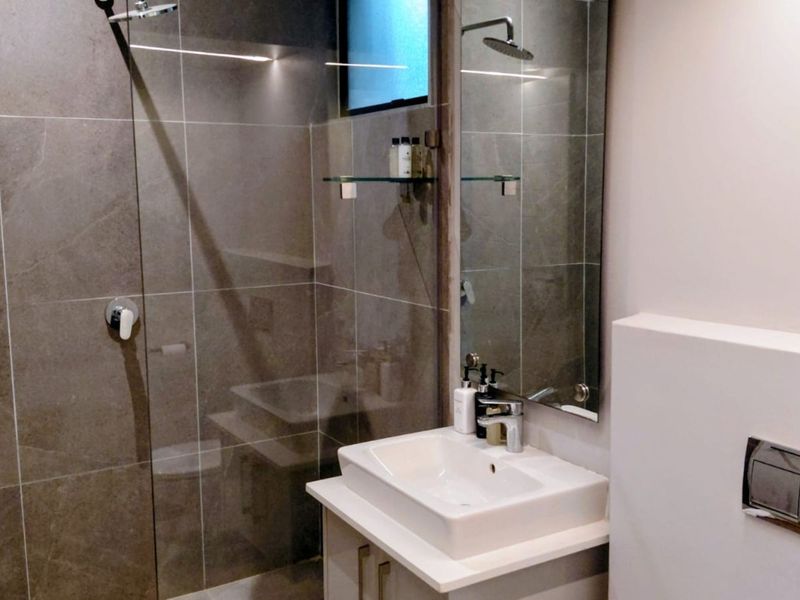 Modern bathroom featuring a walk-in shower with glass screen, contemporary vanity with countertop basin, and a sleek wall-mounted flush plate.