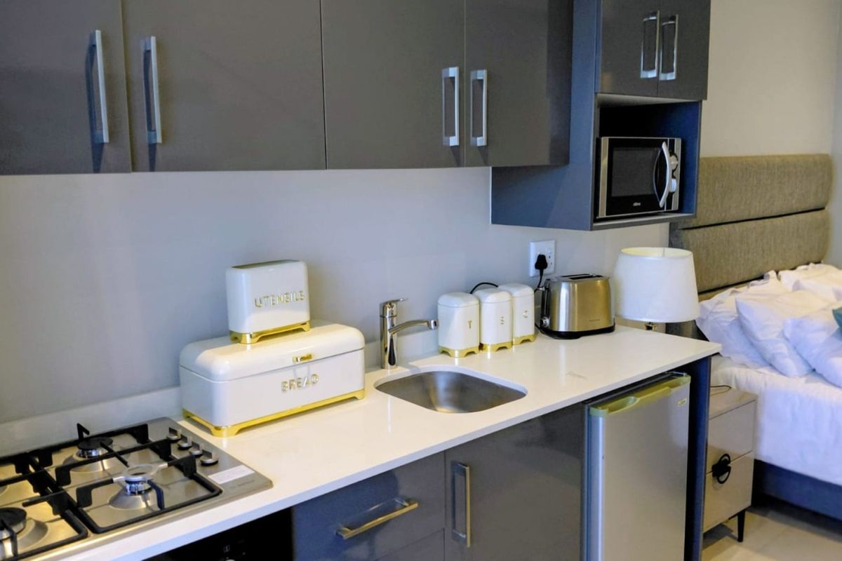 Compact kitchenette featuring modern grey cabinetry, stone countertops, a gas hob, and a built-in microwave, integrated into a studio-style living space.