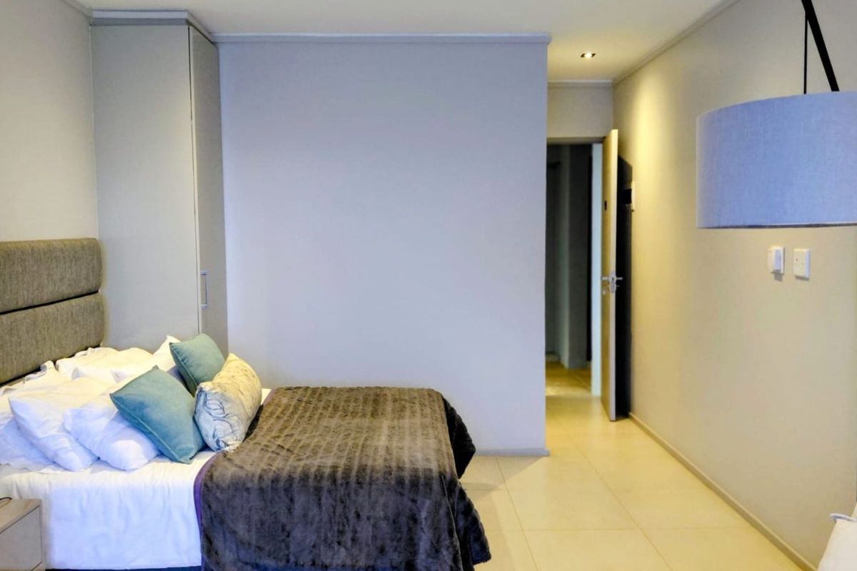 A well-maintained bedroom featuring neutral tiled flooring, recessed ceiling lighting, and a built-in wardrobe, offering a clean and functional living space.