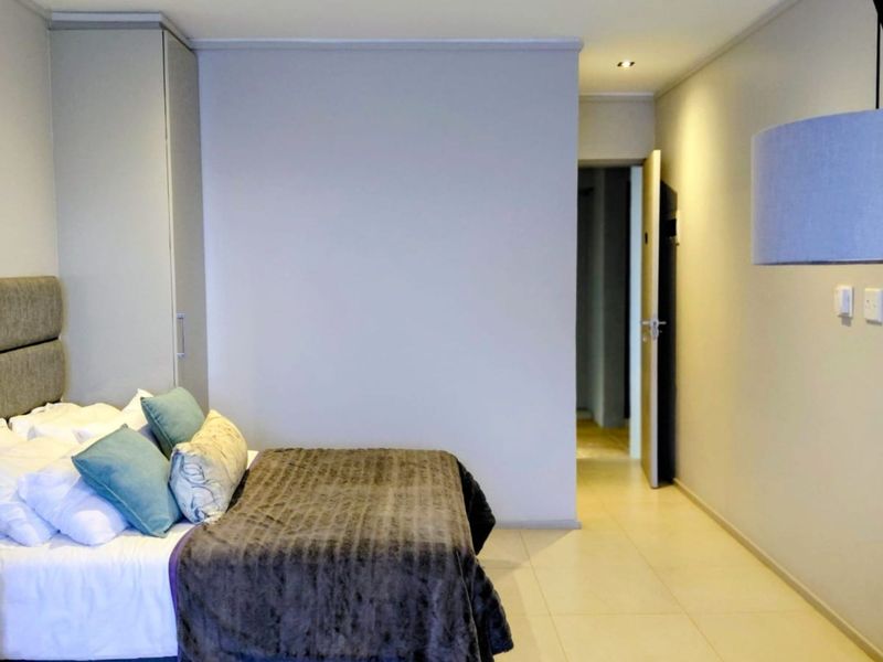 A well-maintained bedroom featuring neutral tiled flooring, recessed ceiling lighting, and a built-in wardrobe, offering a clean and functional living space.