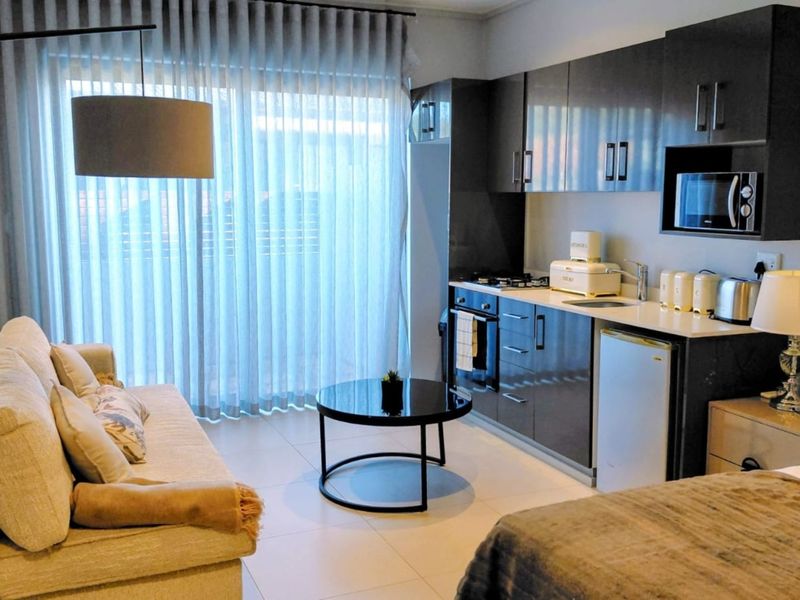 Modern open-plan living area featuring a compact kitchenette with high-gloss cabinetry, integrated appliances, and direct access to a balcony through sliding glass doors.