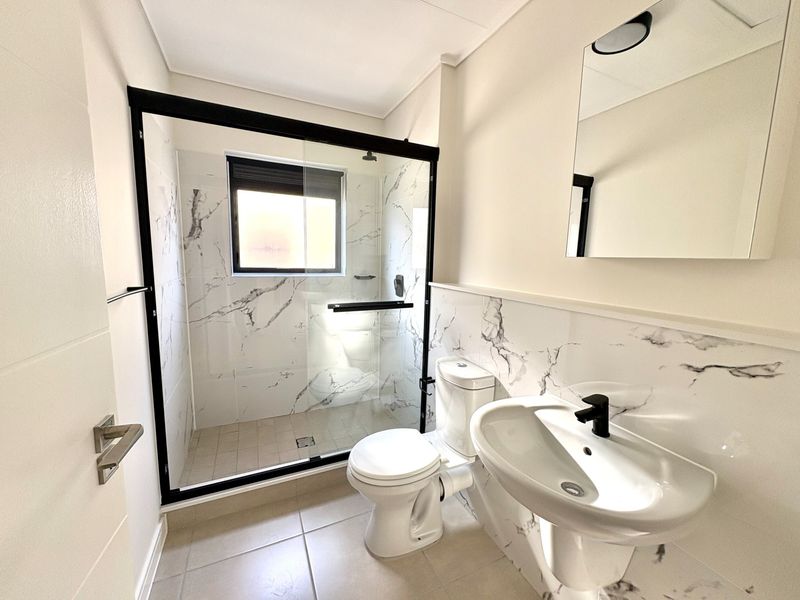 Modern bathroom featuring a walk-in shower with black-framed glass, marble-look wall tiling, pedestal basin with black fixtures, and a wall-mounted mirror.