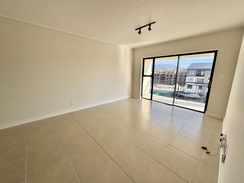 A bright, empty living room featuring neutral tiled flooring, modern track lighting, and a large sliding glass door leading to a balcony.