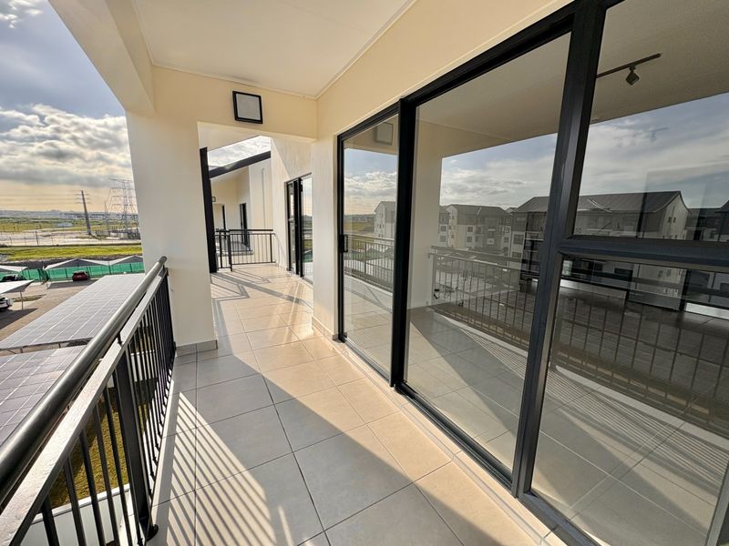 A spacious covered balcony featuring tiled flooring, black metal railings, and large sliding glass doors providing access to the interior.