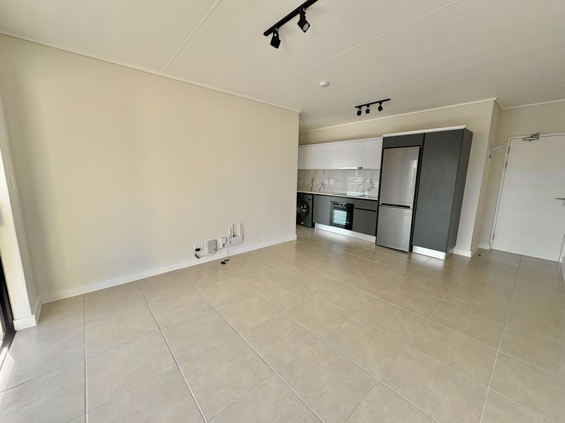 Modern open-plan living area featuring a sleek kitchen with built-in cabinetry, integrated appliances, and neutral tiled flooring throughout.