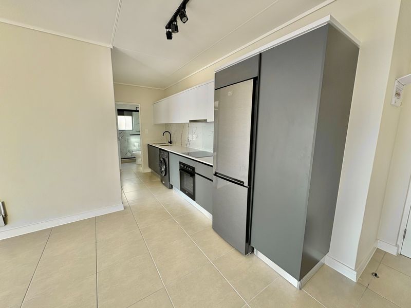 Modern kitchen featuring sleek grey and white cabinetry, integrated appliances, marble-look splashback, and contemporary track lighting, leading into a tiled living area.