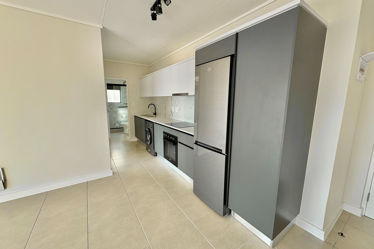 Modern kitchen featuring sleek grey and white cabinetry, integrated appliances, marble-look splashback, and contemporary track lighting, leading into a tiled living area.