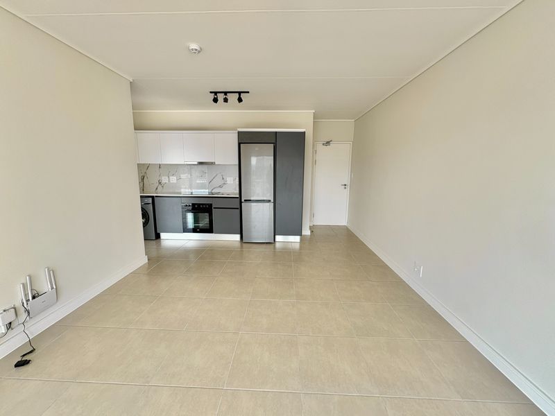 Modern open-plan kitchen and living area featuring sleek cabinetry, marble-look splashback, integrated appliances, and neutral tiled flooring in a clean, vacant space.
