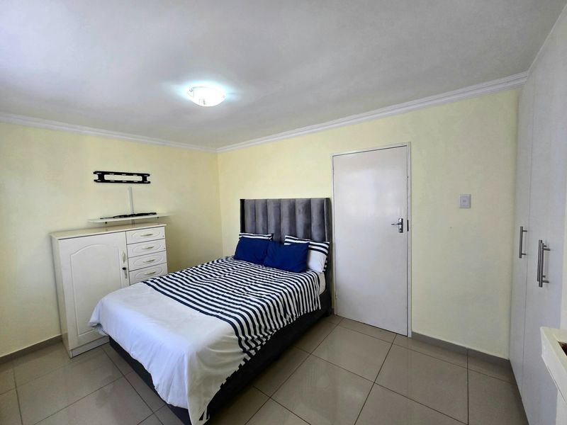 A functional bedroom featuring tiled flooring, built-in cupboards, and neutral wall finishes, providing a clean and practical living space.