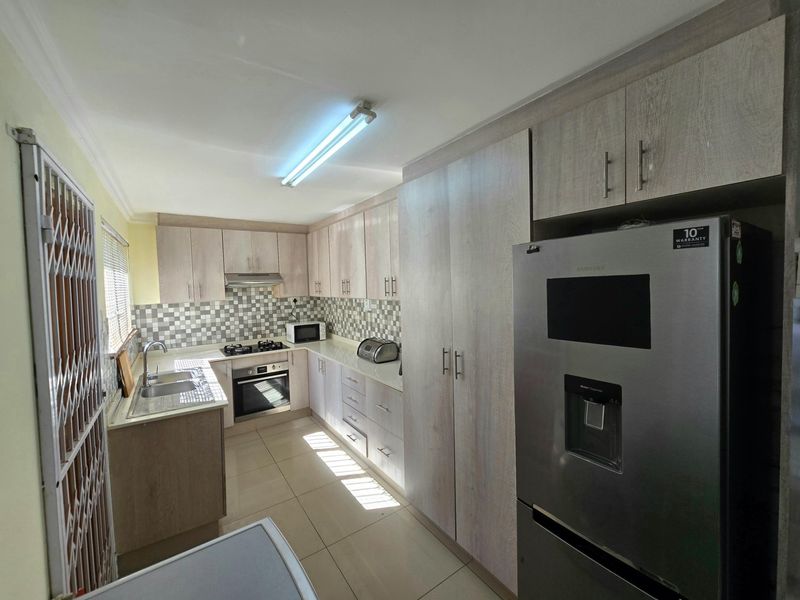 A functional kitchen featuring light wood-finish cabinetry, tiled backsplash, gas hob, built-in oven, and tiled flooring.