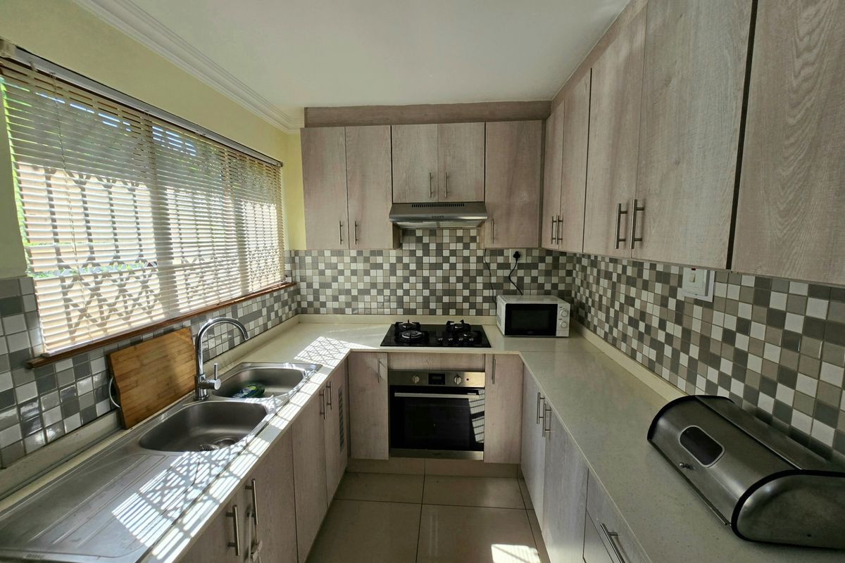 A functional kitchen featuring light wood-grain cabinetry, stone countertops, a gas hob with extractor, and a tiled backsplash with a double sink.
