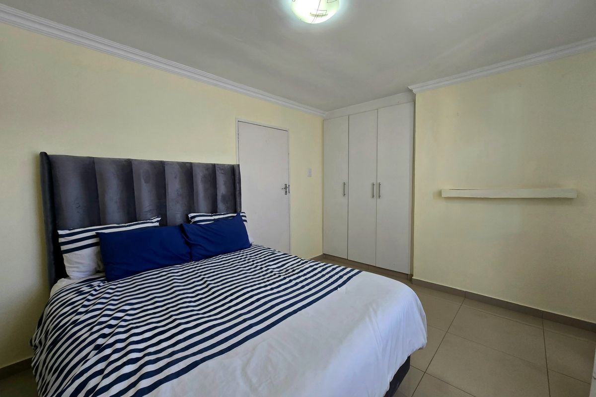A functional bedroom featuring tiled flooring, built-in cupboards, and neutral wall finishes, providing a clean and practical living space.