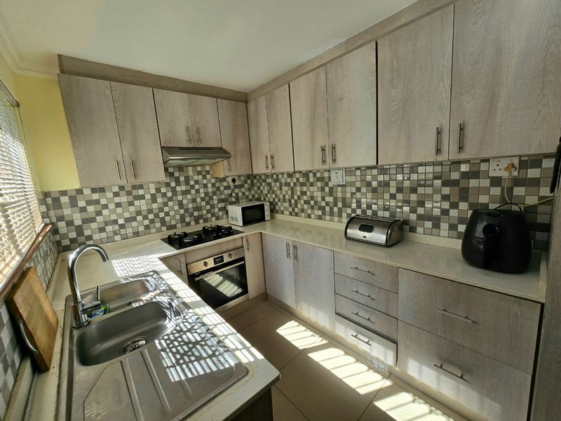 A functional kitchen featuring light wood-look cabinetry, stone countertops, a mosaic tile backsplash, and integrated stainless steel appliances including an oven and gas hob.
