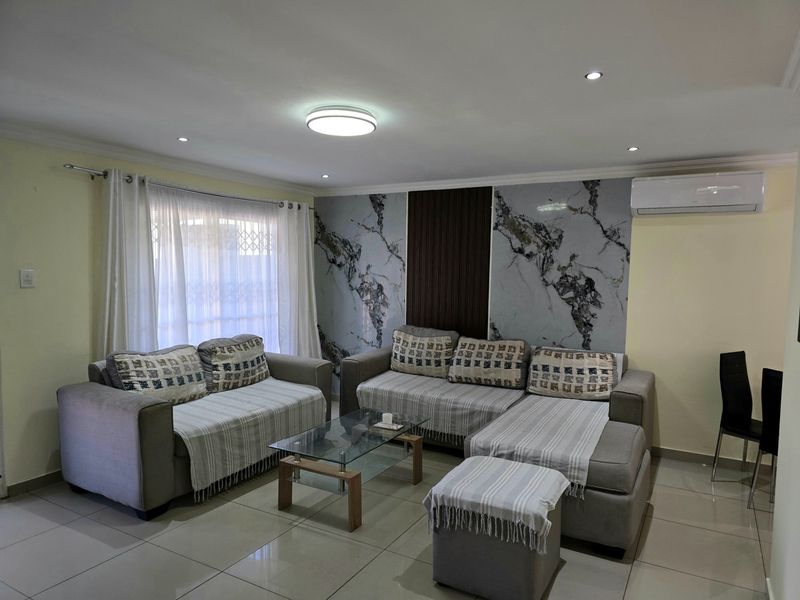 A well-maintained living room featuring tiled flooring, recessed lighting, a split-system air conditioner, and a decorative marble and timber slat feature wall.