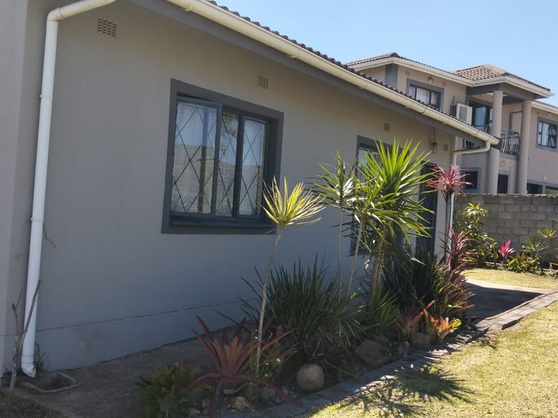 A view of the rear exterior of the house featuring a paved walkway, landscaped garden beds, and security-fitted windows.