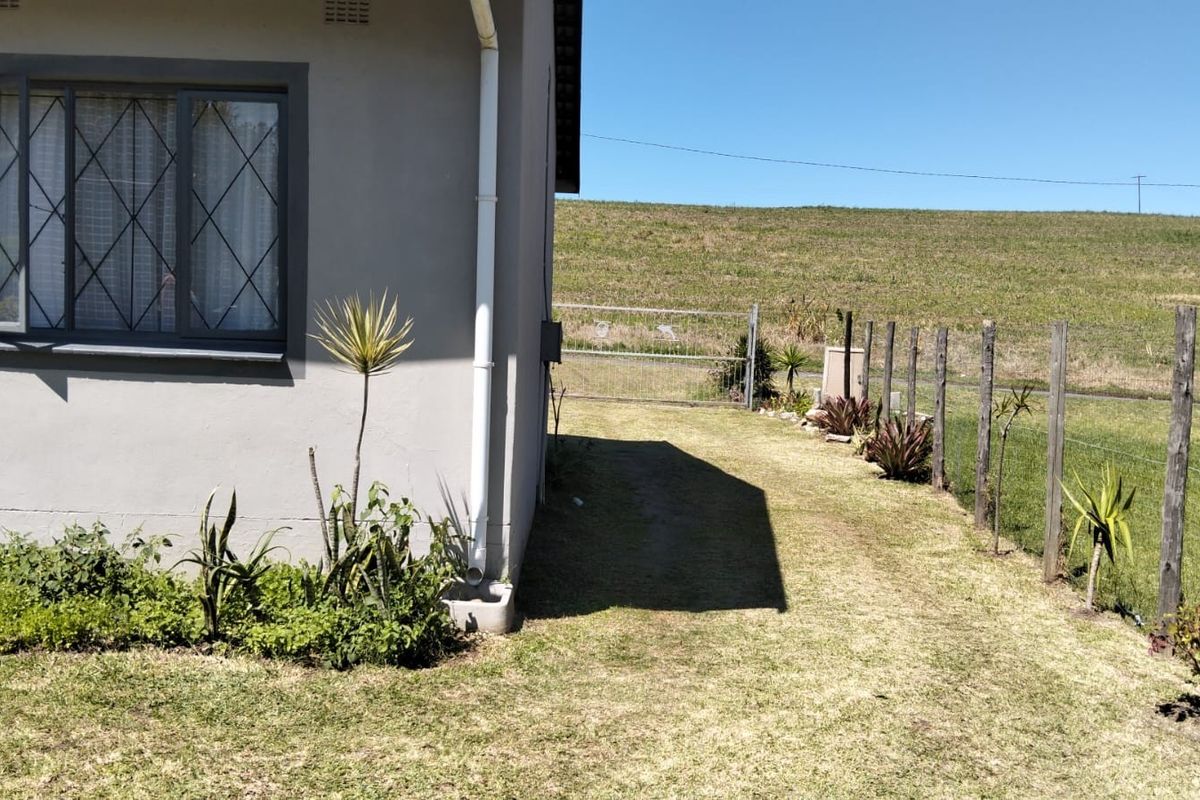 A view of the side and rear exterior of the house featuring a lawn, wire fencing, and a downpipe.