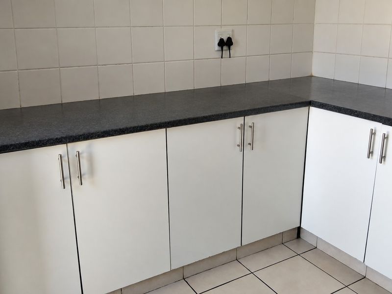 A clean, functional kitchen corner featuring white cabinetry, dark laminate countertops, and neutral ceramic wall and floor tiling.