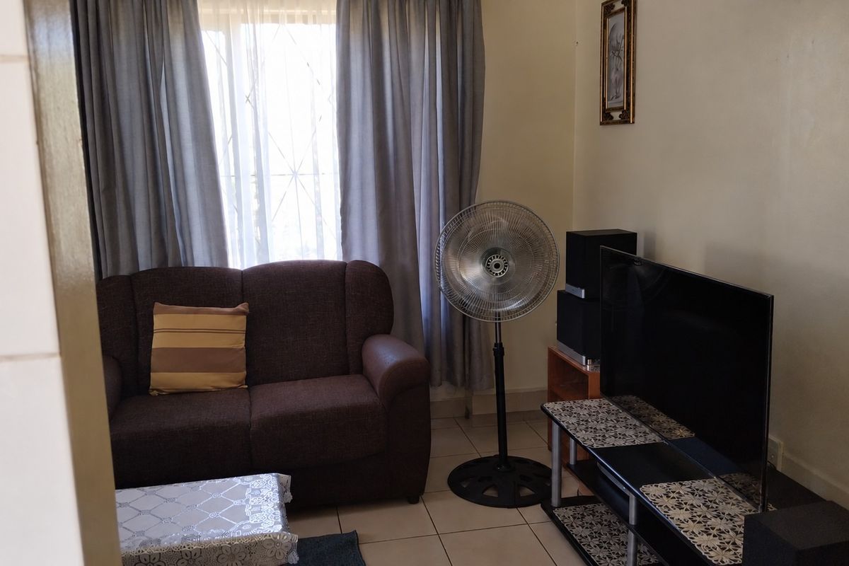 A functional living room featuring tiled flooring and large windows with curtain rails, providing a comfortable and well-lit space.