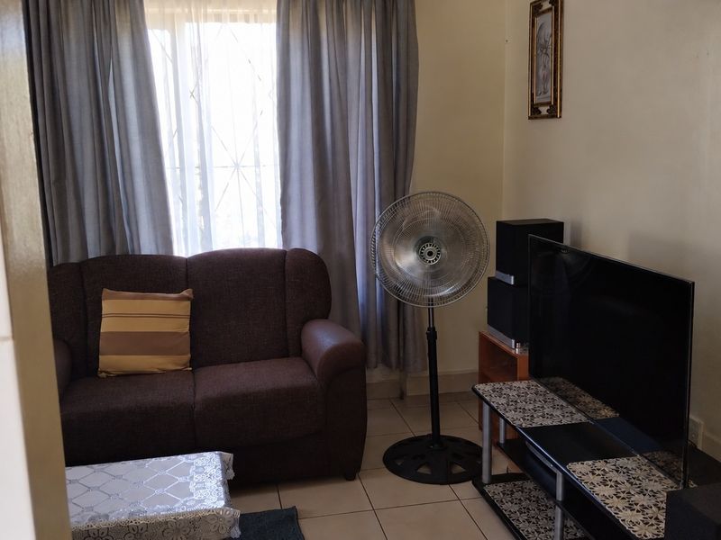 A functional living room featuring tiled flooring and large windows with curtain rails, providing a comfortable and well-lit space.
