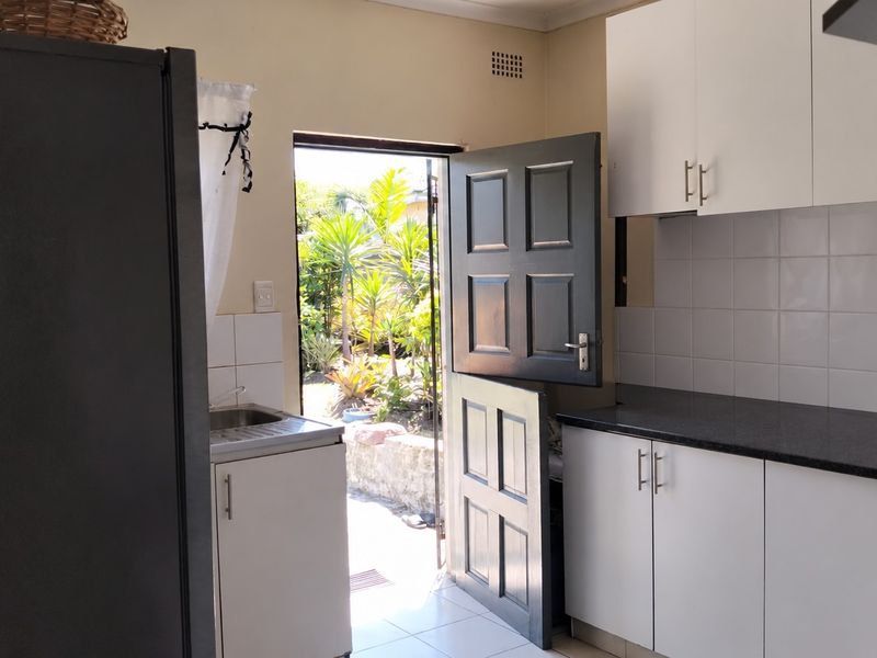 A functional kitchen featuring white cabinetry, dark granite countertops, tiled backsplash, and a stable door providing direct access to the garden.