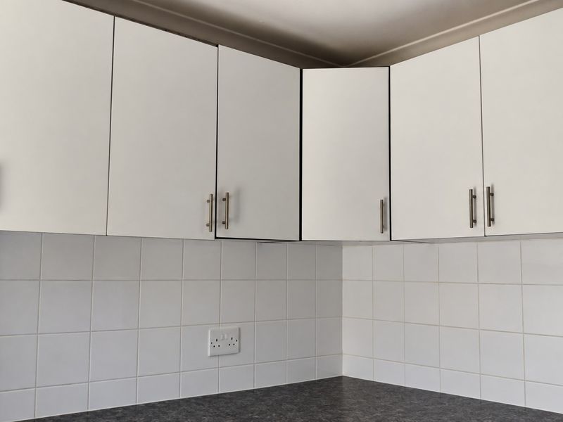 A clean kitchen corner featuring white upper cabinetry, a dark laminate countertop, and a white tiled backsplash with integrated electrical outlets.
