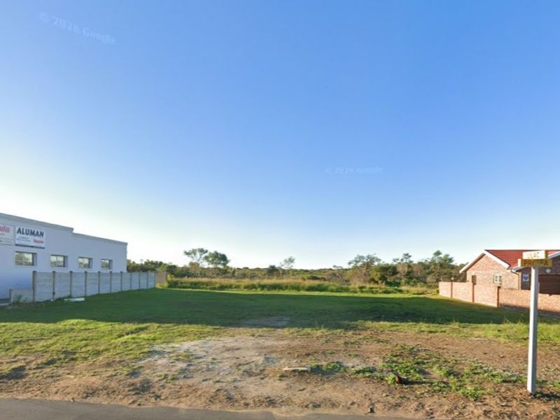 A vacant commercial land plot featuring grassed terrain, enclosed by a combination of precast concrete and brick boundary walls.