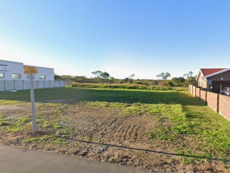 A vacant commercial land plot featuring level ground, boundary walls, and street access, situated between existing commercial and residential properties.