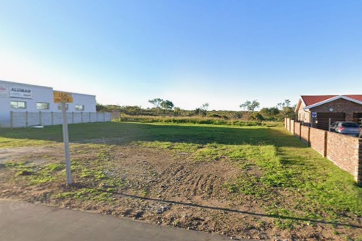 A vacant commercial land plot featuring level ground, boundary walls, and street access, situated between existing commercial and residential properties.