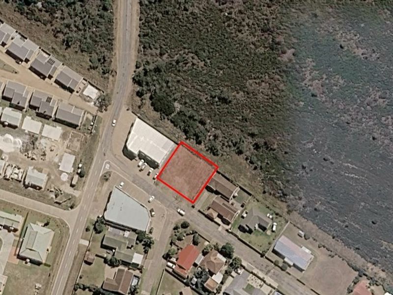 Aerial view of a vacant commercial land plot highlighted in red, situated in a developed area with nearby road access.