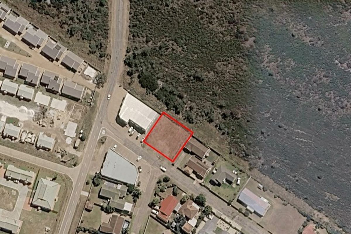 Aerial view of a vacant commercial land plot highlighted in red, situated in a developed area with nearby road access.