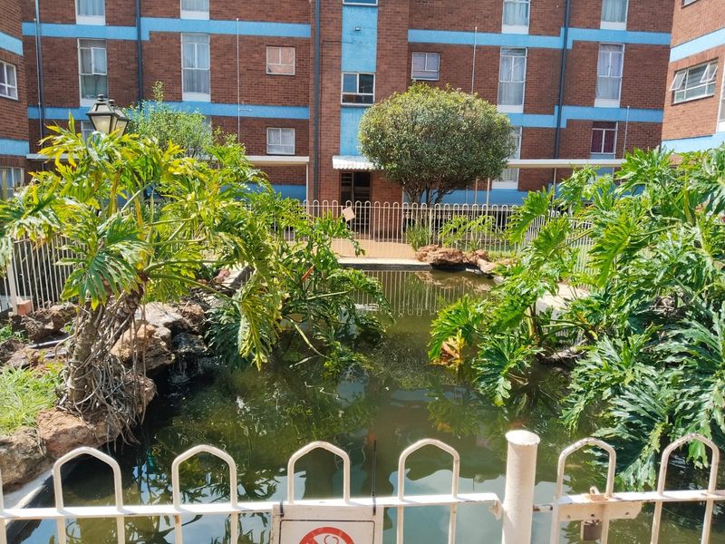 A communal outdoor area featuring an ornamental pond and landscaped garden set against a brick apartment building facade.