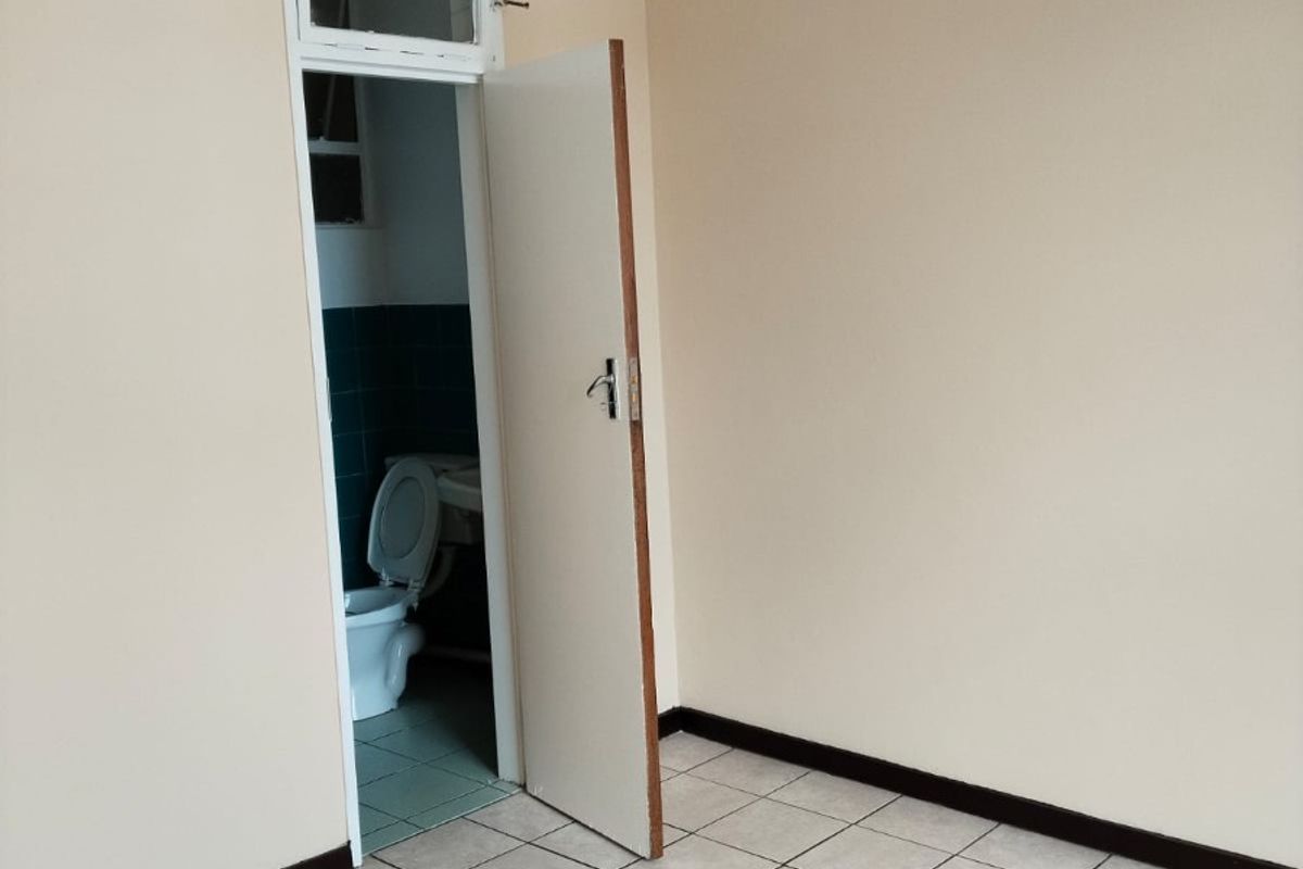 An empty bedroom featuring neutral wall paint, tiled flooring, and direct access to an en-suite bathroom.
