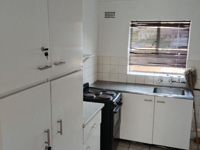 A compact kitchen featuring white built-in cabinetry, a stainless steel sink, tiled backsplash, and tiled flooring, offering a functional space ready for modernization.