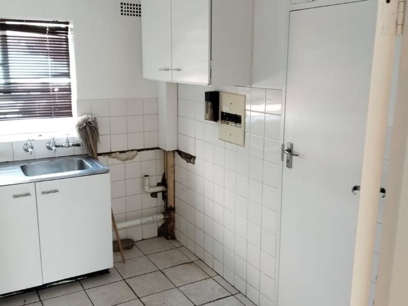 A small kitchen area featuring tiled flooring, a sink, and wall-mounted cabinetry, currently requiring repairs to the wall tiling and exposed plumbing infrastructure.