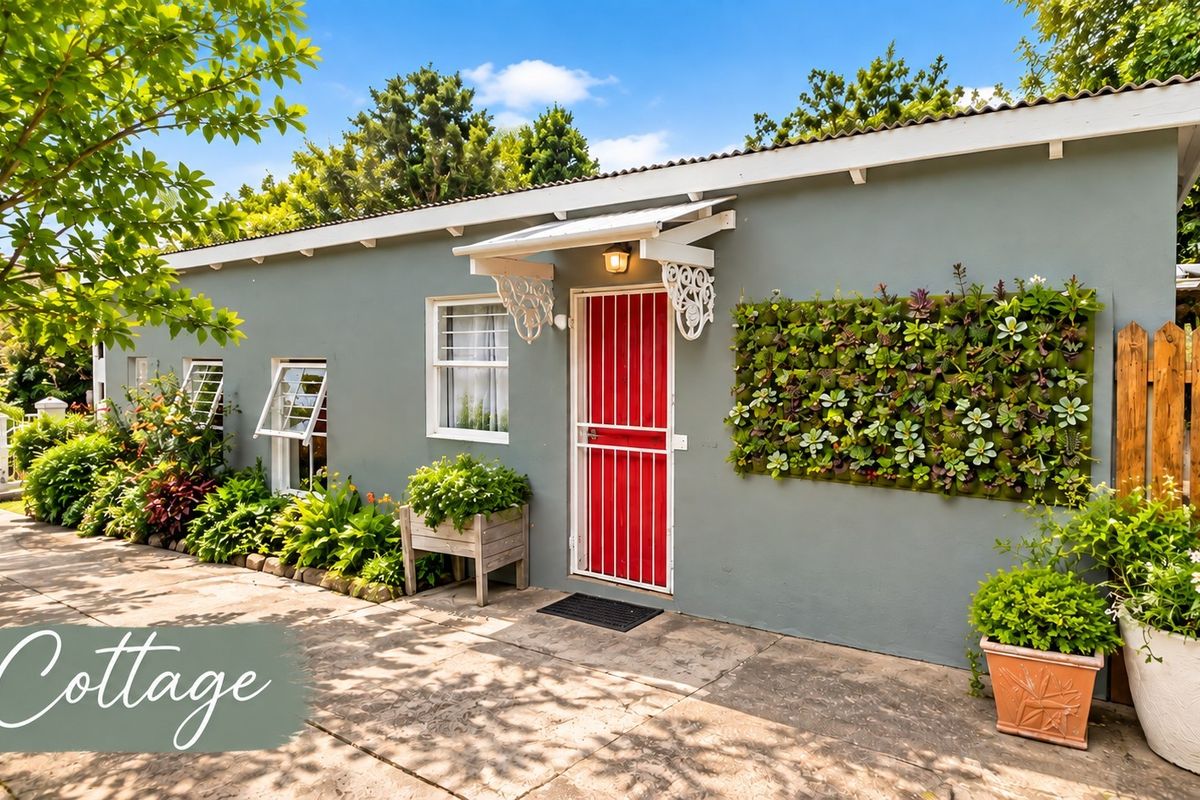 A charming cottage exterior featuring a red security gate, decorative awning, and a vibrant vertical garden wall set against a paved patio area.