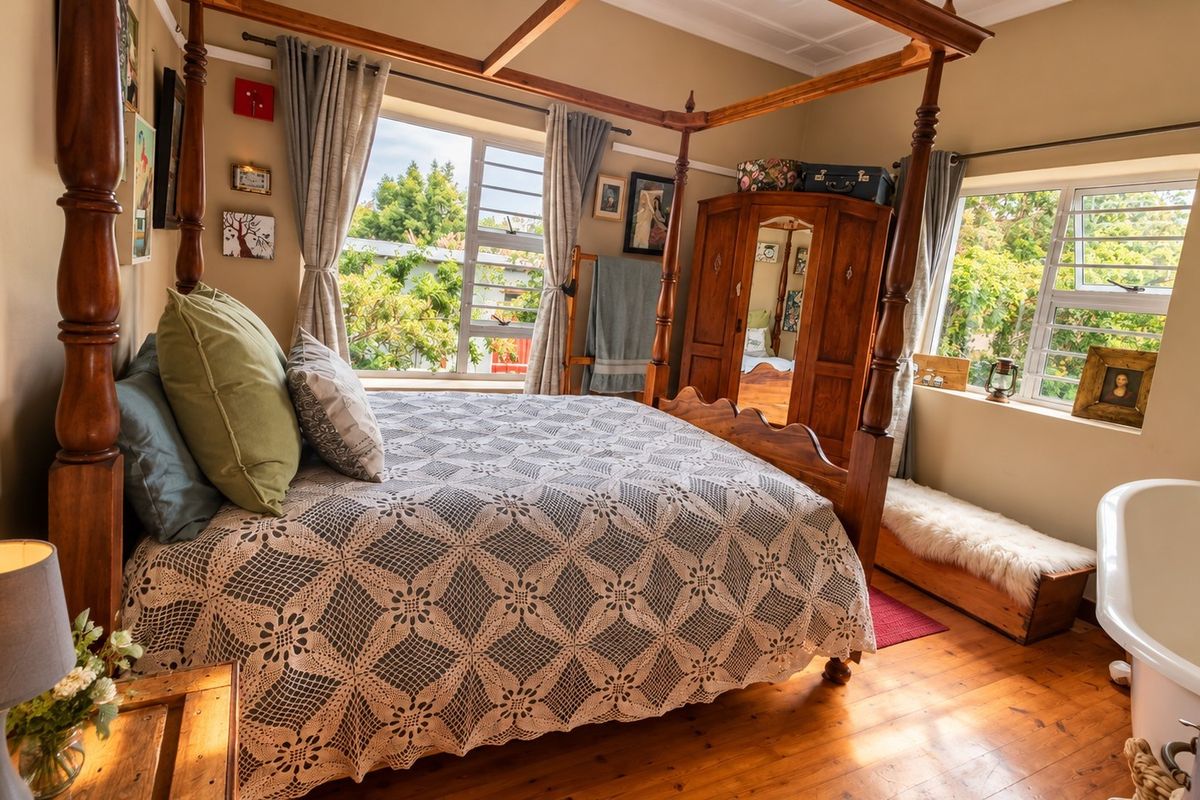 A bedroom featuring timber flooring, aluminium window frames, and a unique integrated freestanding bathtub within the sleeping area.