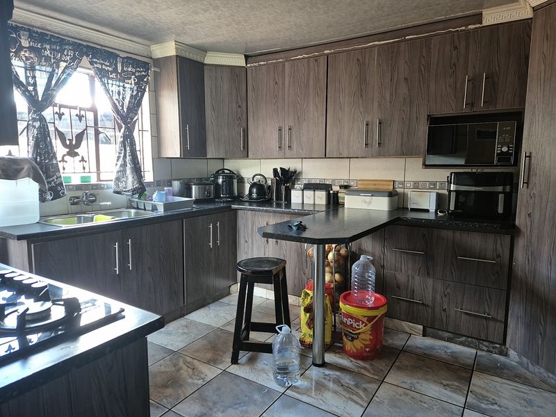 A functional kitchen featuring wood-look laminate cabinetry, dark countertops, a breakfast bar, and ceramic floor tiles.