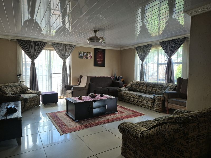 A spacious living room featuring glossy ceiling panels, tiled flooring, and large sliding glass doors that provide natural light.