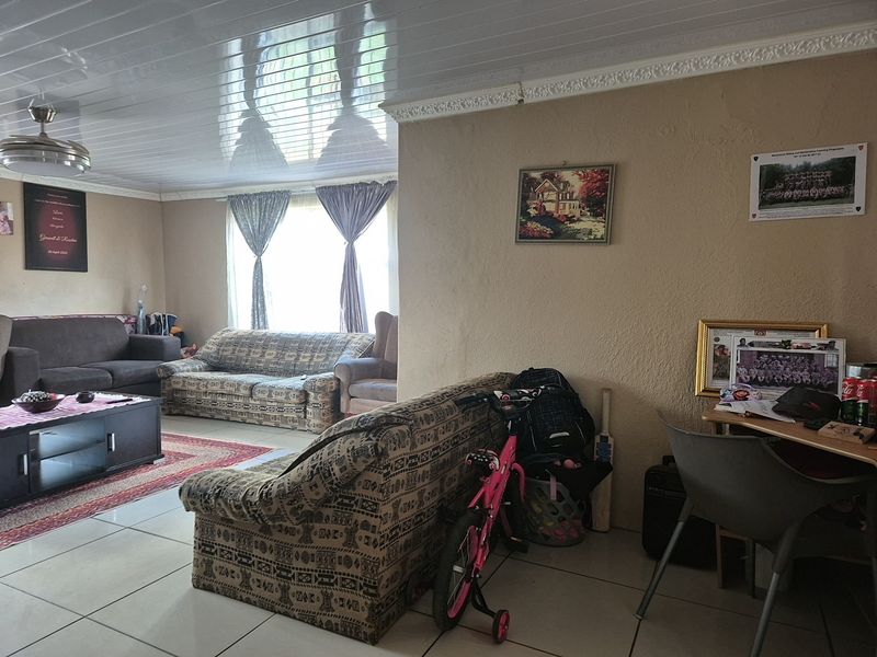 A living room featuring tiled flooring, a glossy PVC ceiling, and a ceiling fan, with visible wall texture and plaster imperfections.