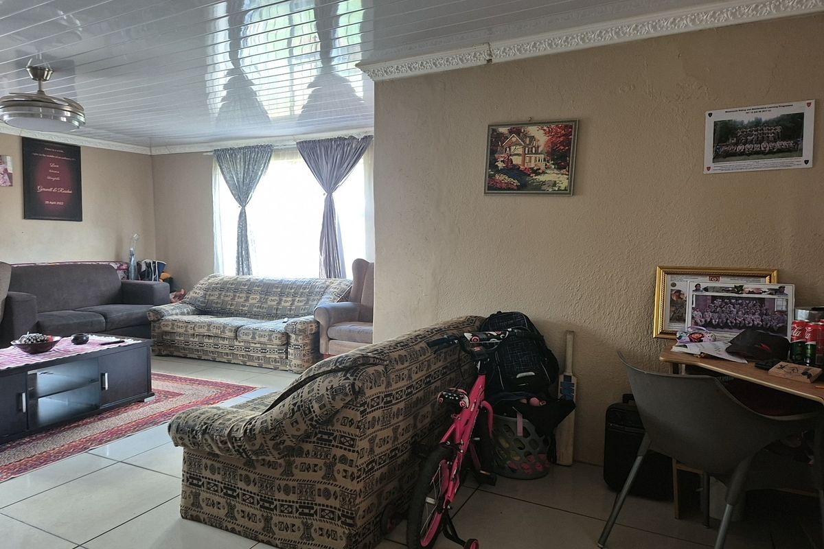 A living room featuring tiled flooring, a glossy PVC ceiling, and a ceiling fan, with visible wall texture and plaster imperfections.