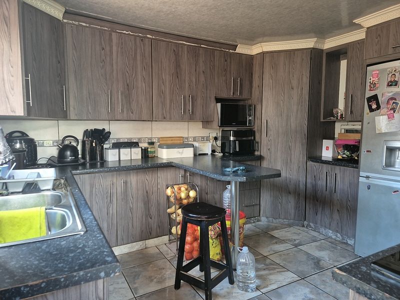 A functional kitchen featuring wood-grain laminate cabinetry, dark countertops, a double stainless steel sink, and tiled flooring with integrated microwave space.