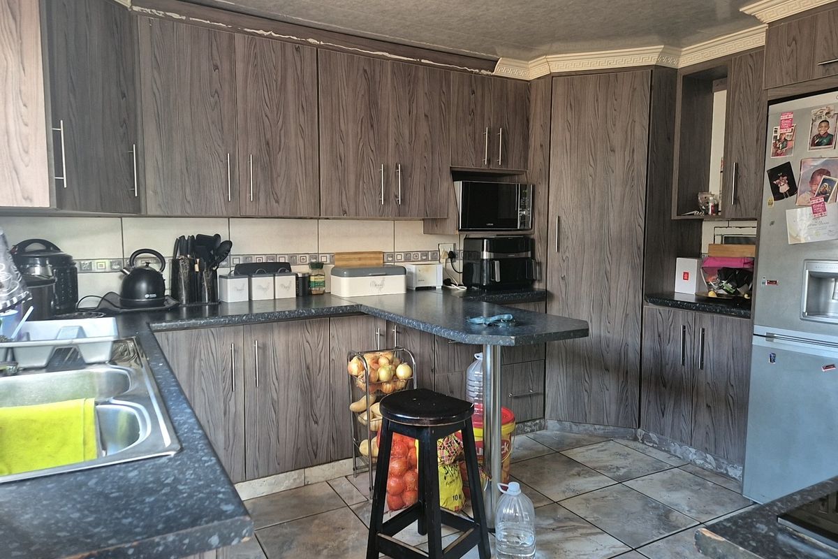 A functional kitchen featuring wood-grain laminate cabinetry, dark countertops, a double stainless steel sink, and tiled flooring with integrated microwave space.