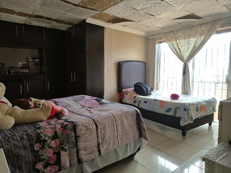 A bedroom featuring built-in cupboards, tiled flooring, and a sliding glass door, currently showing signs of ceiling and wall damage requiring maintenance.