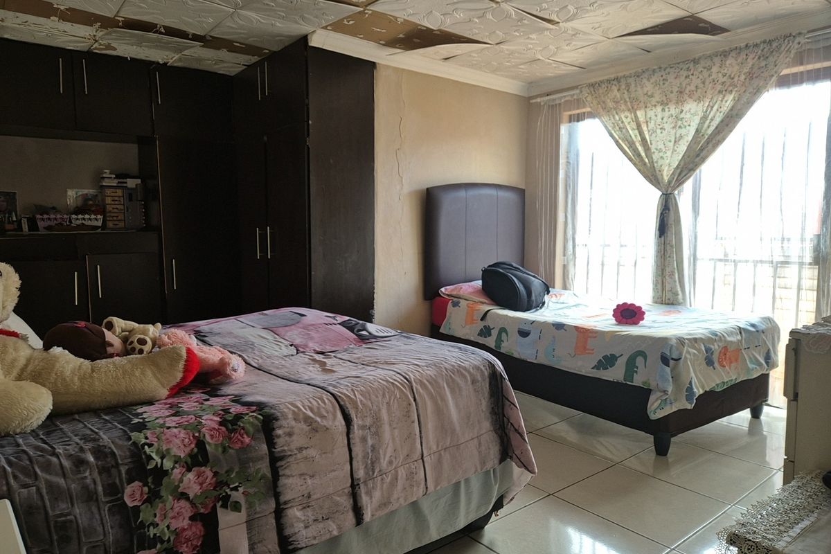 A bedroom featuring built-in cupboards, tiled flooring, and a sliding glass door, currently showing signs of ceiling and wall damage requiring maintenance.