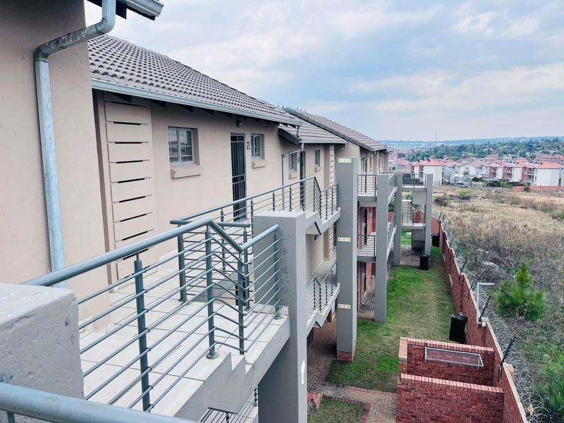 Exterior view of an apartment complex featuring multi-level tiled balconies with metal railings, overlooking a landscaped garden and surrounding residential area.